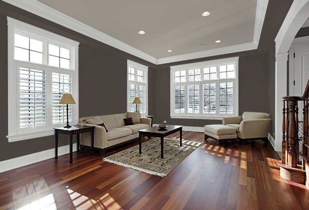 Modern living room with a beige sofa, armchair, dark wood coffee table, and large windows.