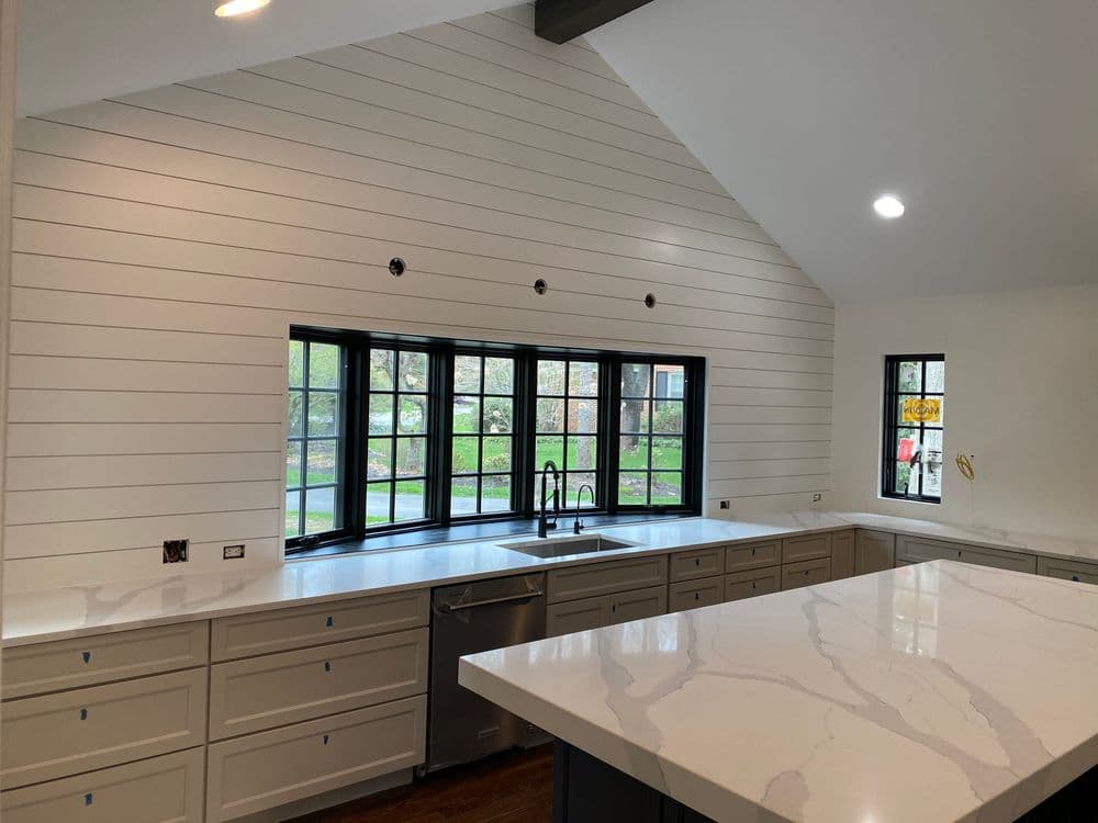 Modern kitchen with white shiplap walls, large windows, and a marble countertop.