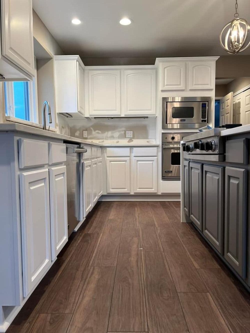 Modern kitchen with white cabinets, stainless steel appliances, and wooden flooring.
