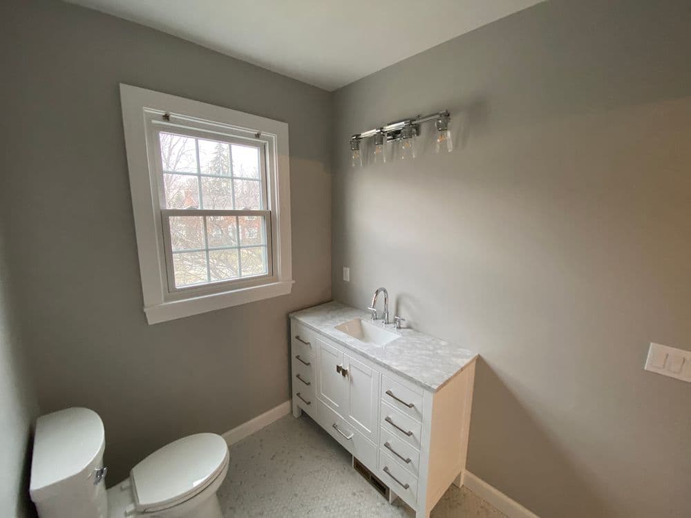 Modern bathroom with gray walls, white vanity, and window for natural light.