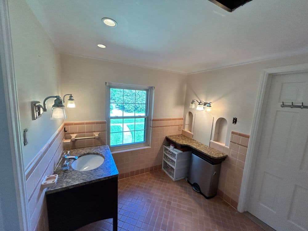 Spacious bathroom with granite countertop, window, and pink tile accents.